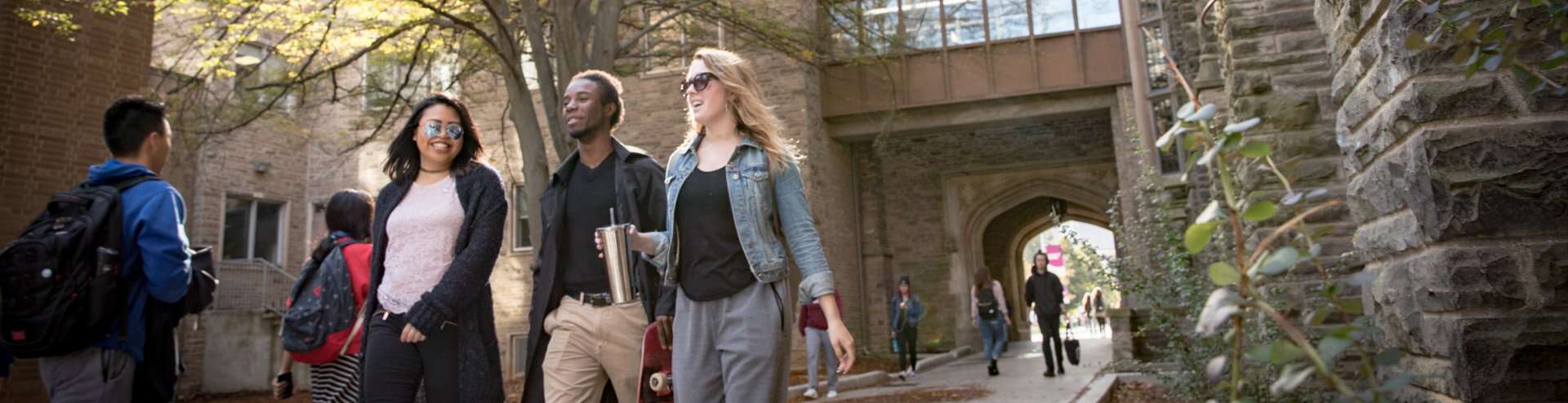 Three students smiling and talking while walking down the pathway beside University Hall.